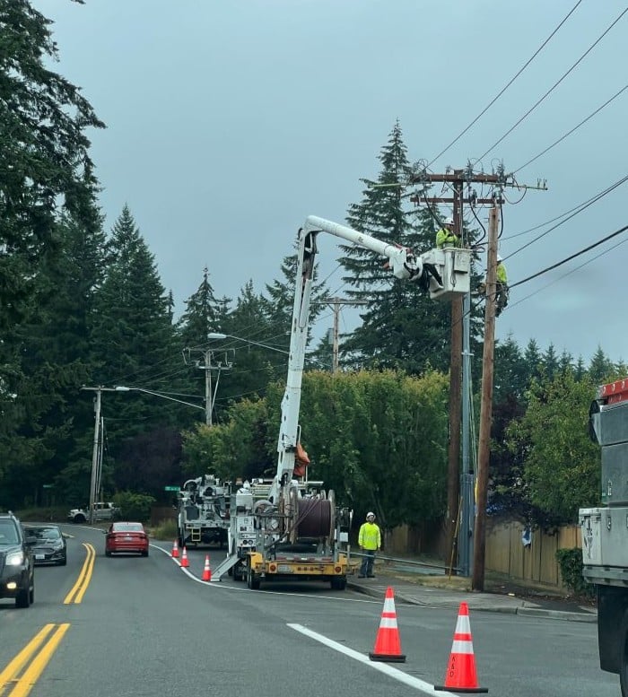 Utility crews working from bucket trucks to repair overhead power lines along a roadside following a service disruption.